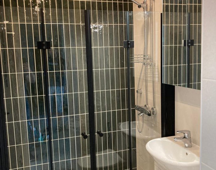 Kylpyhuone, jossa on mustavalkoiset pystylaatat, lasiseinä ja suihkukaappi.